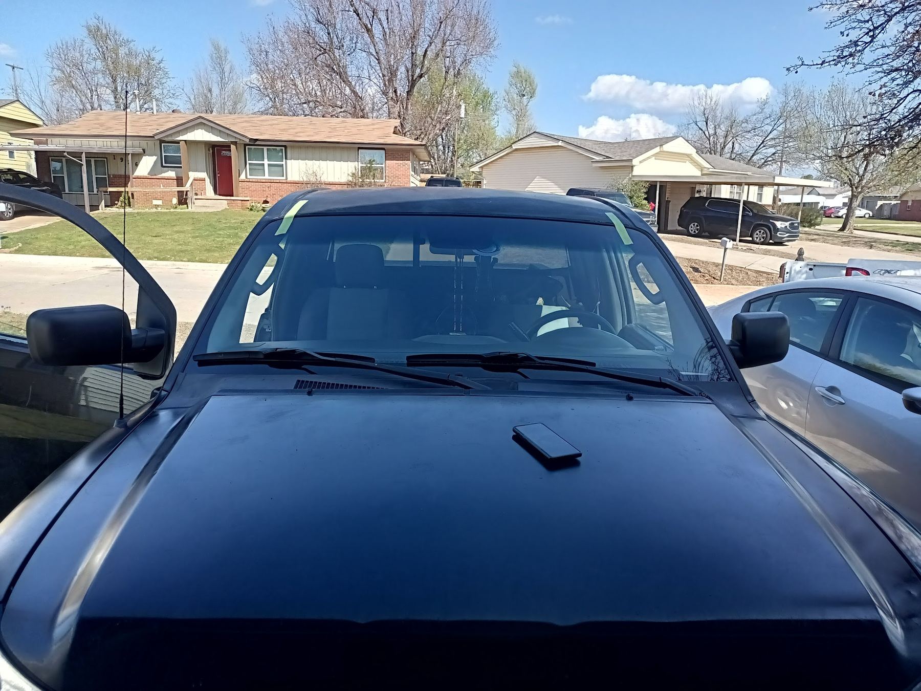 Dark pickup with a new windshield, taped at the top, parked in a residential driveway