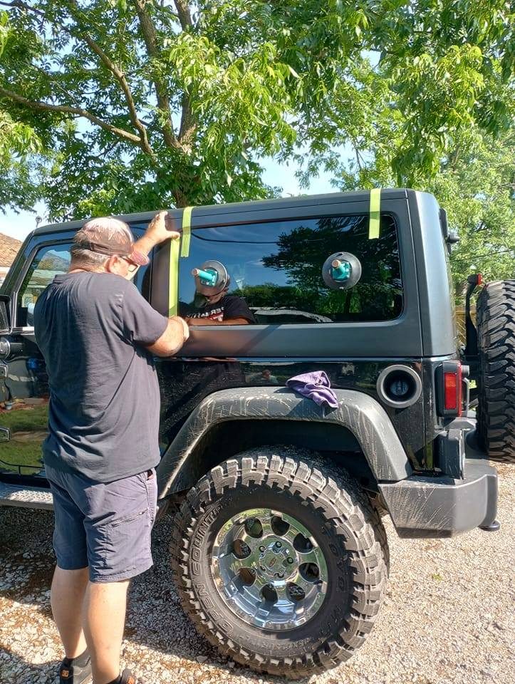 Technician pressing and taping a freshly set side window on a Jeep Wrangler